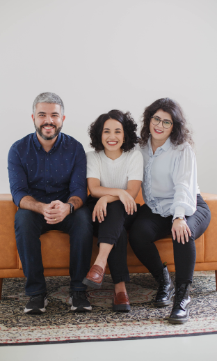 Francisco, Marina e Duda sentados em um sofá sorrindo.